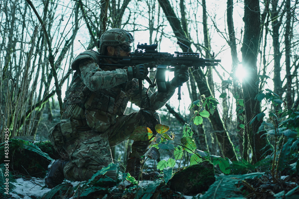 Obraz premium Portrait of airsoft player in professional equipment in helmet aiming at victim with gun in the forest. Soldier with weapons at war