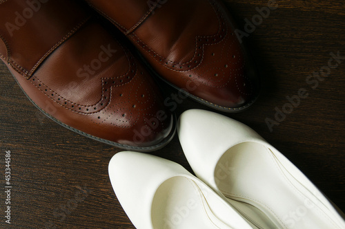 Brown men's shoes and white women's shoes on a dark wooden background, top view
