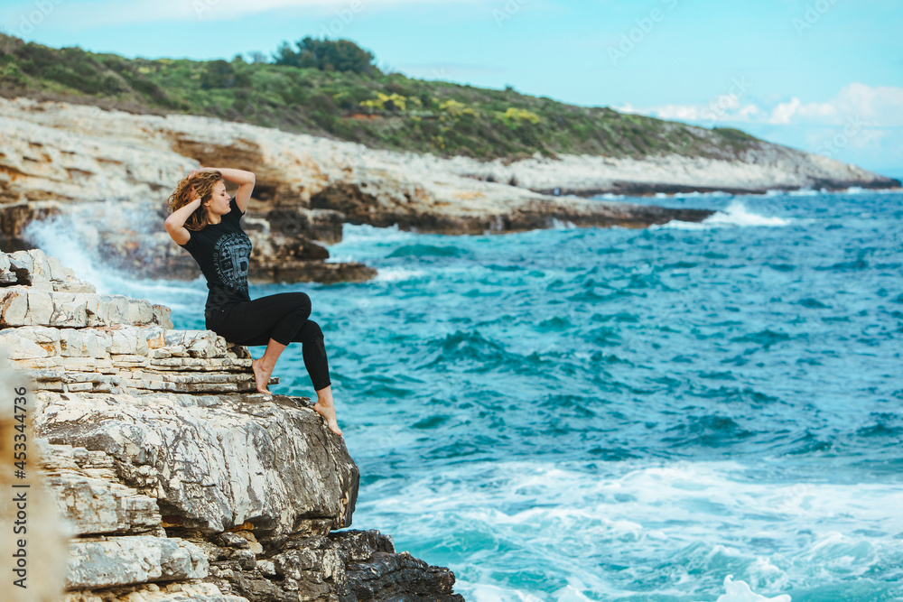 Obraz premium young slim woman sitting on the cliff edge looking at sea