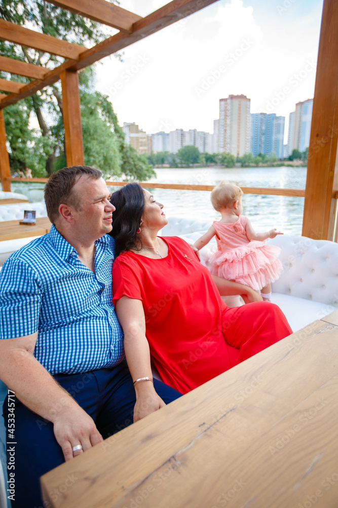 Beautiful married couple and lovely little daughter sitting together on the sofa on the background of a summer park in the city