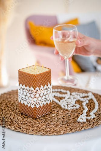 Handmade wax candle with white lace ribbon. Romantic setting. Hand with a glass of sparkling wine. photo