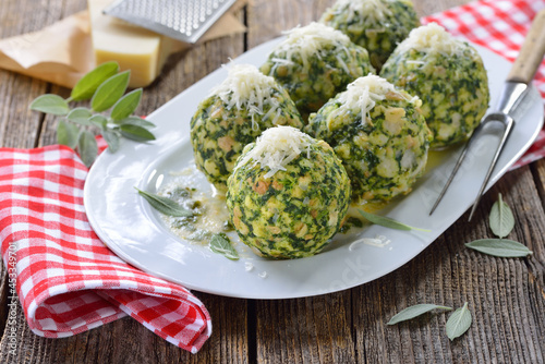 Deftige hausgemachte Südtiroler Spinatknödel mit gebräunter Salbei-Butter und Parmesen auf weißer Platte serviert - South Tyrolean spinach bread dumplings with melted sage butter and parmesan cheese