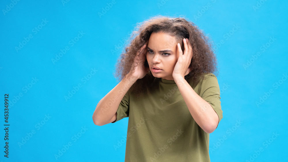 Stressed or unhappy african american girl touching her head suffering from headache wearing olive t-shirt isolated on blue background. Beauty concept. Health care concept. Stressed or unhappy african american girl touching her head suffering from headache wearing olive t-shirt isolated on blue background. Beauty concept. Health care concept.