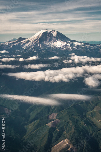 View of Mount Rainier from a plane in the sky. Clouds surround the mountain and it's peak is covered in snow. 