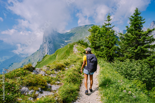 A woman with a backpack stands on top of a mountain, The girl travels to beautiful places, Reaching the goal, mountain ridge at Saxer Lucke, Kreuzberg in Alpstein Appenzell Innerrhoden Switzerland.  photo