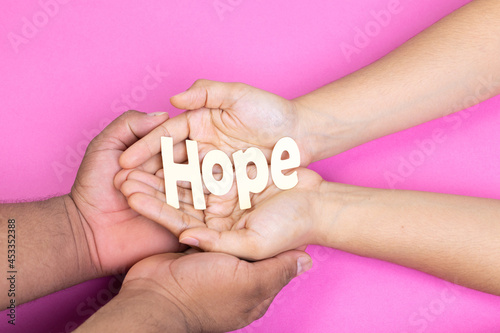 two hands holding word hope, breast cancer, pink background