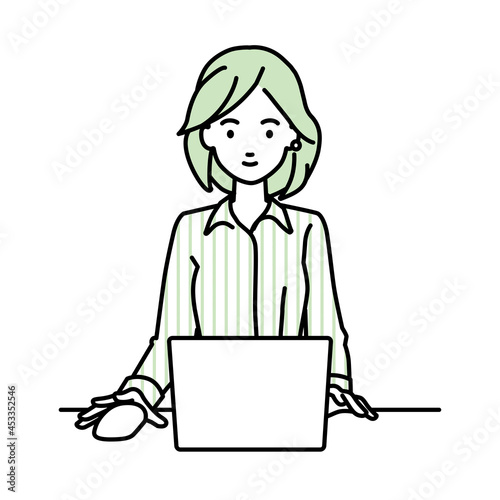 デスクで座ってPCを使っているブラウスの女性