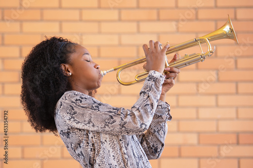 Young afro american woman playing the trumpet with her eyes closed on a brick wall background