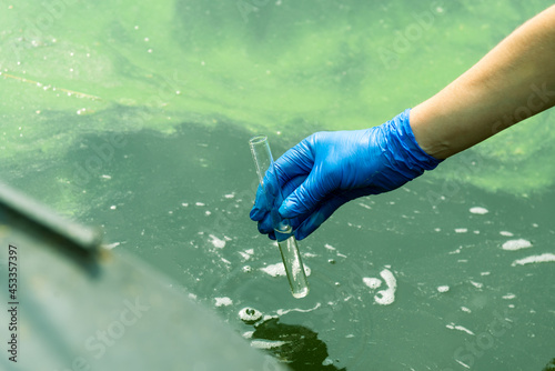 A gloved hand takes water into a test tube from a city reservoir. Urban waste water. Sampling from open water. Scientist or biologist takes a sample of water into a test tube