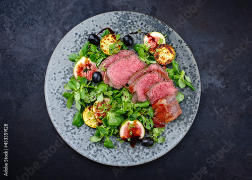 Modern style traditional fried dry aged angus beef filet medaillons with vegetable and lambs lettuce served as top view on a Nordic design plate
