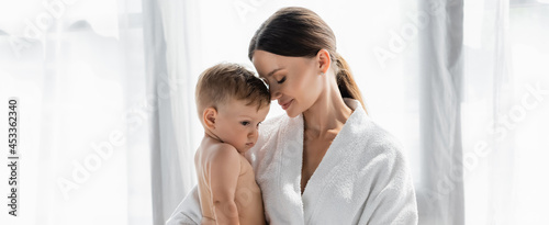 caring mother in bathrobe holding in arms naked toddler son, banner