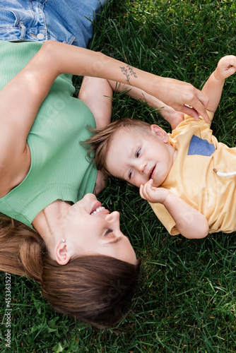 top view of cheerful mother spending time with happy toddler son while lying on grass