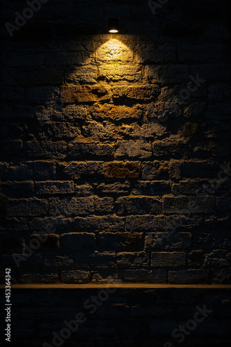 Dark room wall with ceiling light background. Old, weathered grey brick stone wall. Low key, scary, moody space. Room in basement. Vertical, copy space