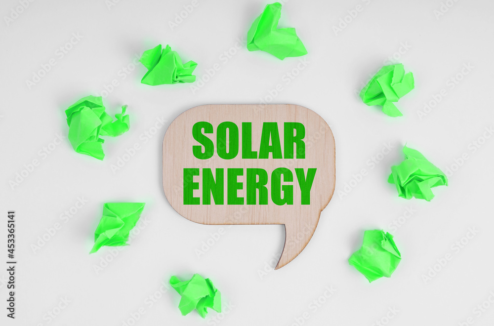 On a white background, there are crumpled green pieces of paper and a wooden sign with the inscription - Solar Energy On a white background, there are crumpled green pieces of paper and a wooden sign with the inscription - Solar Energy