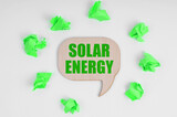 On a white background, there are crumpled green pieces of paper and a wooden sign with the inscription - Solar Energy