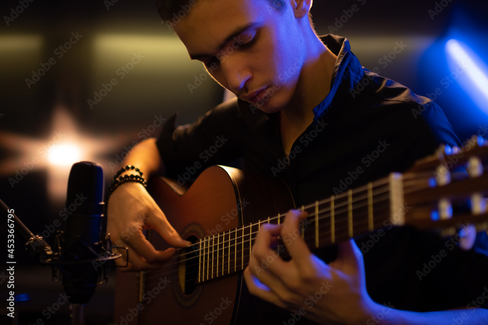 Fototapeta premium Man with a classical guitar in a neon glow. Teenager plays guitar. Young man plays a musical instrument.
