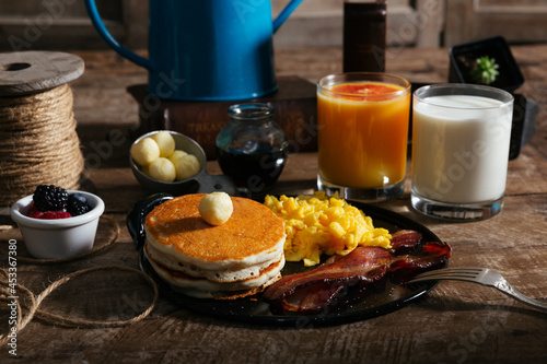 Pancake stack, eggs, bacon, syrup, milk, cup of fruit