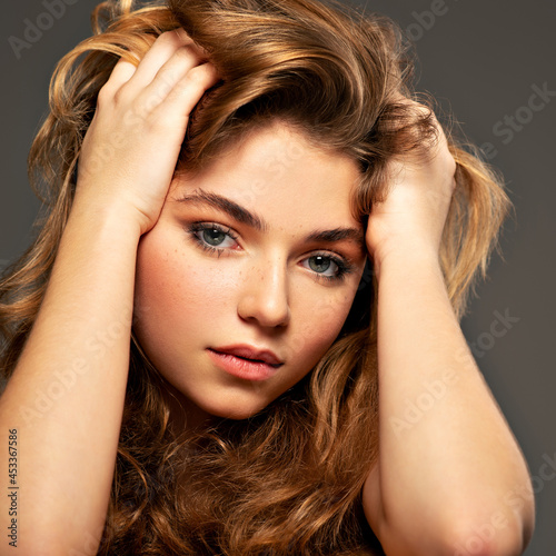 Closeup portrait of an young adult girl with long curly hair. Photo of a fashion model posing at studio. Pretty young woman with long brown hair looking at camera. Beauty portrait.