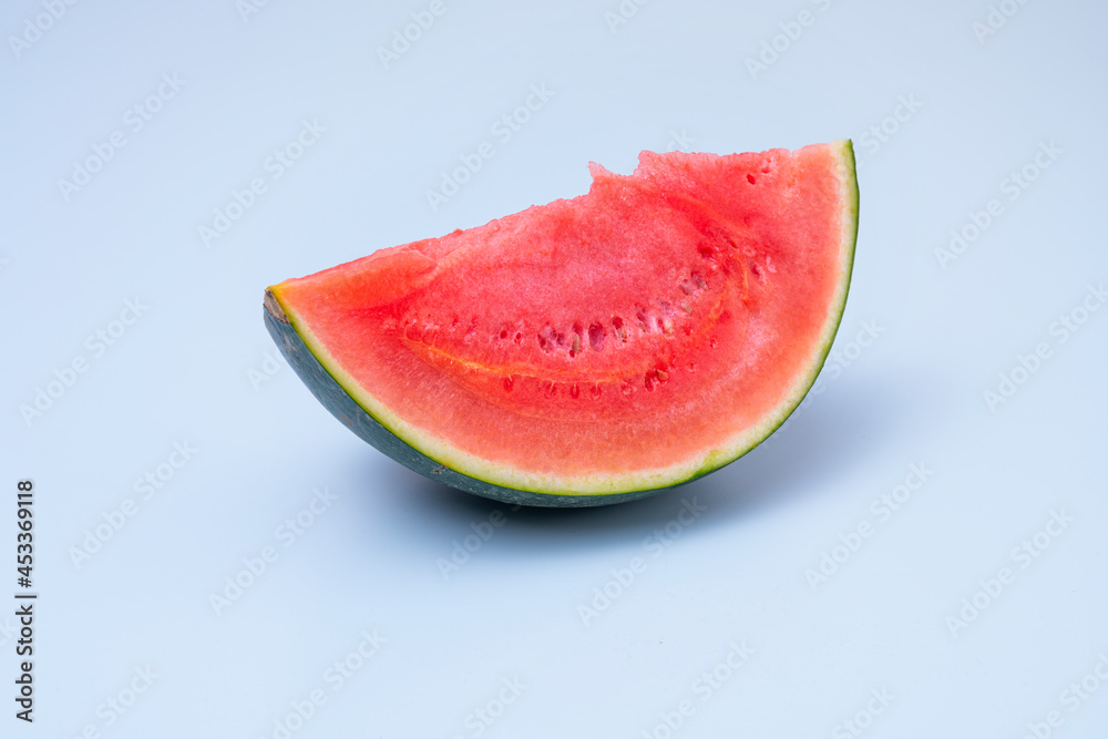 Piece of red watermelon without seeds resting on its green rind on blue background Piece of red watermelon without seeds resting on its green rind on blue background