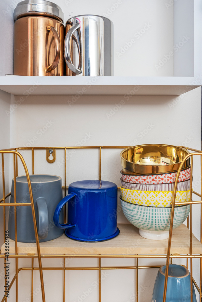 metal and wood shelves with porcelain, metal and enamel mugs small colorful and gold bowls