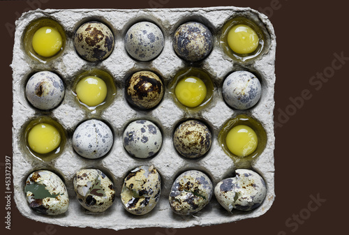 Whole quail eggs and yolks in a paper form on a brown background.