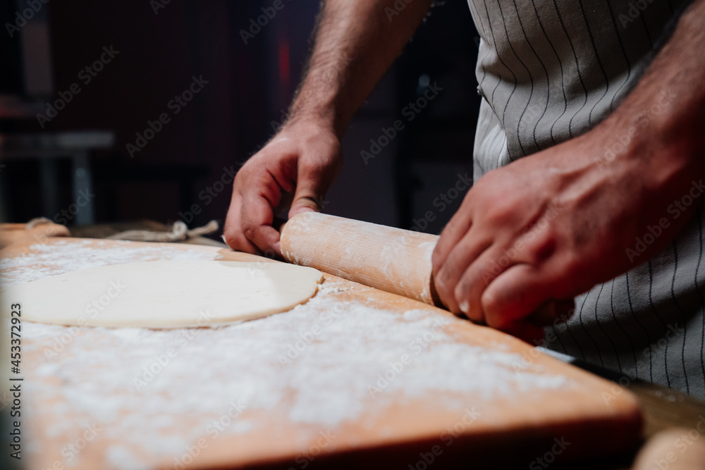 hands roll the dough into a thin layer. Cooking pizza, noodles or pitta at home hands roll the dough into a thin layer. Cooking pizza, noodles or pitta at home