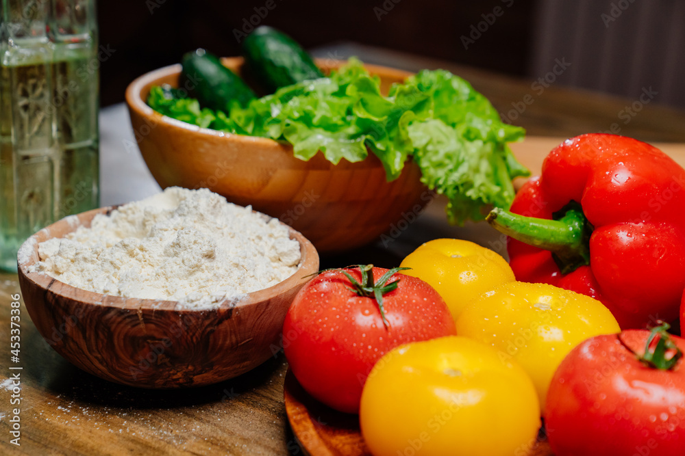 a wooden bowl of flour and vegetables on the kitchen table.