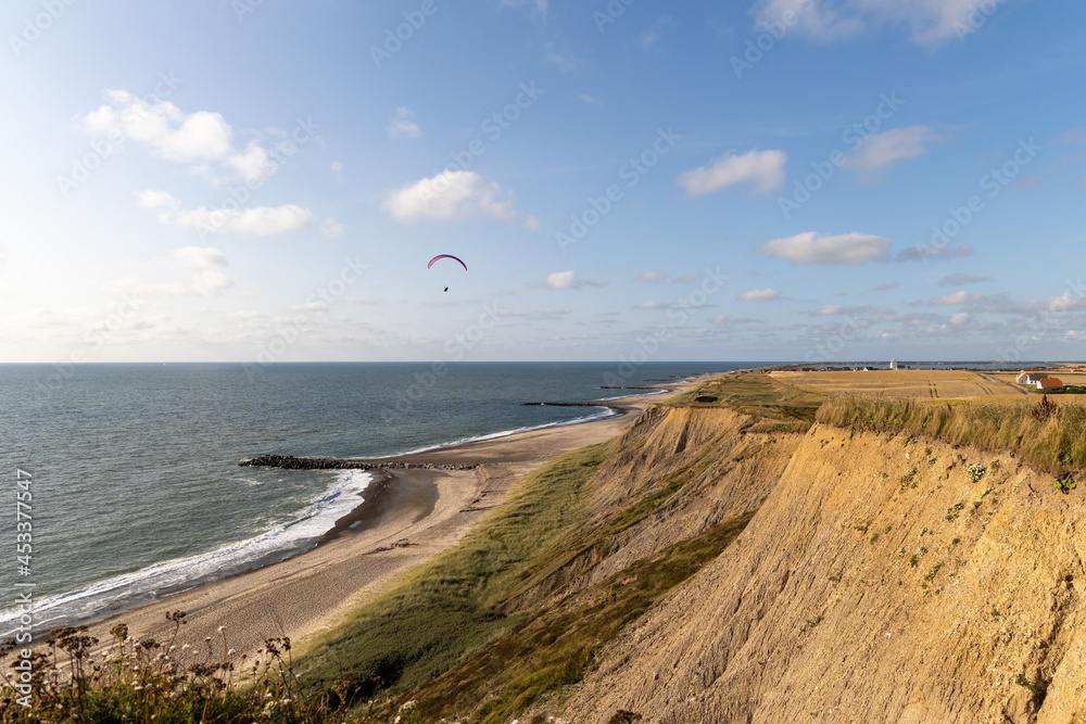 Paraglider soaring along the cliffs of Bovbjerg, Denmark during sunset.  Scenic view from top of the cliffs onto the sea
