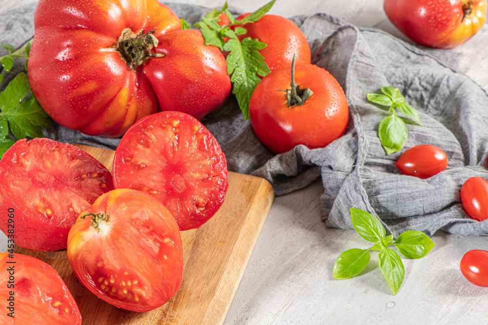 Large variety of tomatoes on rustic kitchen counter. Preparation of tomato sauce with onions and basil