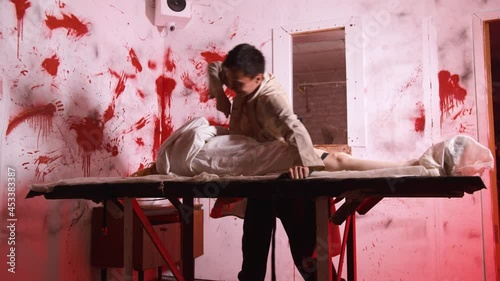 Horror acting - the doctor ties the mad girl to the table in the bloody room of mental hospital photo