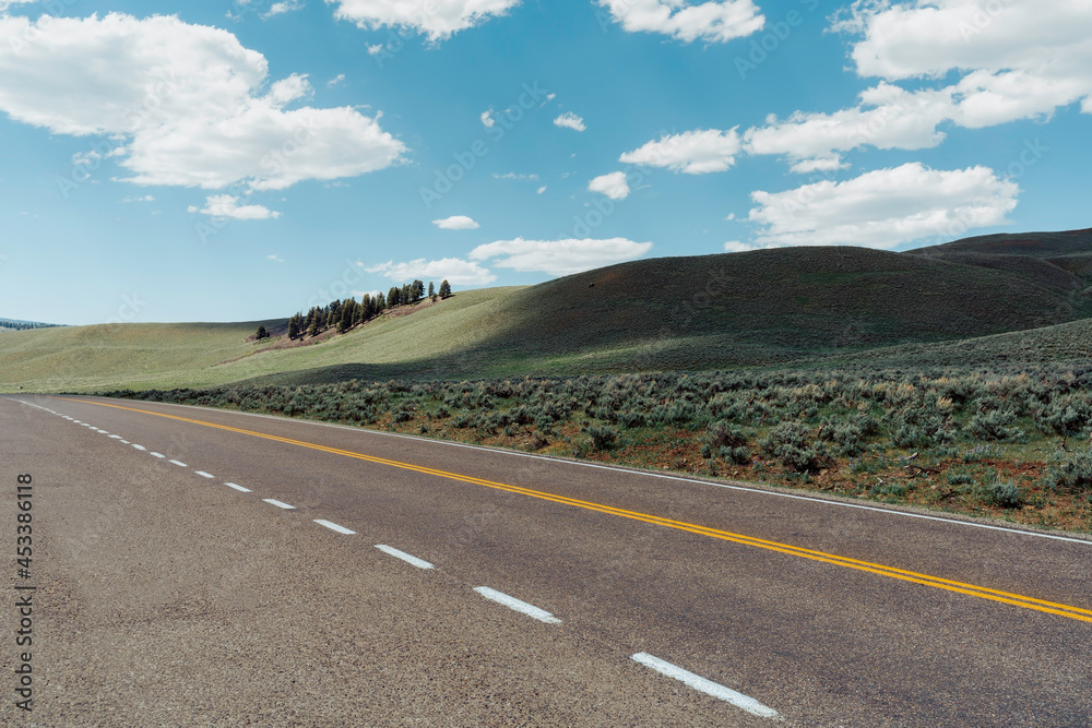 Empty asphalt road with hills and blue sky in Montana