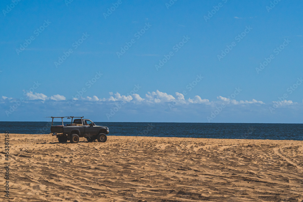 Off road vehicle on sandy beach against blue sky and ocean Off road vehicle on sandy beach against blue sky and ocean