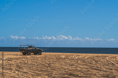 Off road vehicle on sandy beach against blue sky and ocean