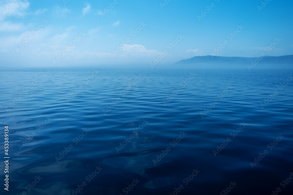 Waves on surface of water with cloudy sky and mountain. Copy space