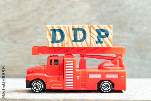 Fire ladder truck hold letter block in word DDP (Abbreviation of Delivered duty paid) on wood background photo