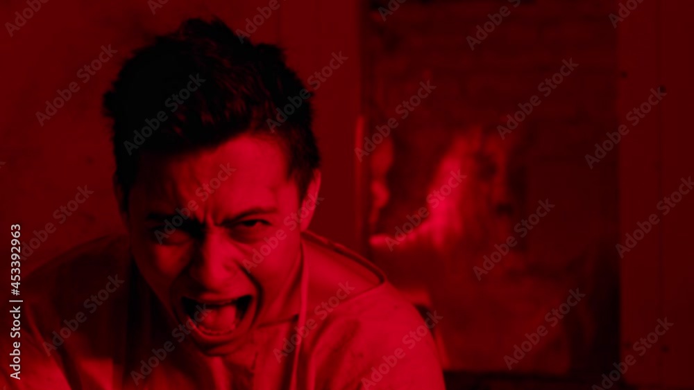 Mad man sitting in the mental hospital in straitjacket and screaming with a scary girl on the background Mad man sitting in the mental hospital in straitjacket and screaming with a scary girl on the background