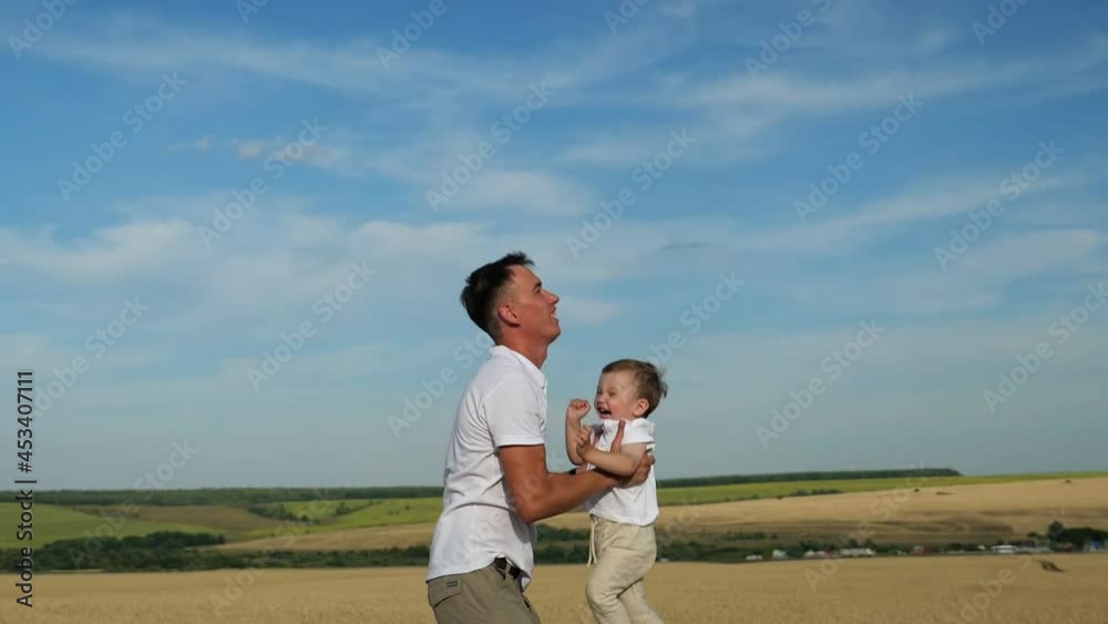 Father tosses toddler son in yellow wheat field and boy laughs happily in dad arms on sunny day against rural landscape under blue sky, slow motion Father tosses toddler son in yellow wheat field and boy laughs happily in dad arms on sunny day against rural landscape under blue sky, slow motion