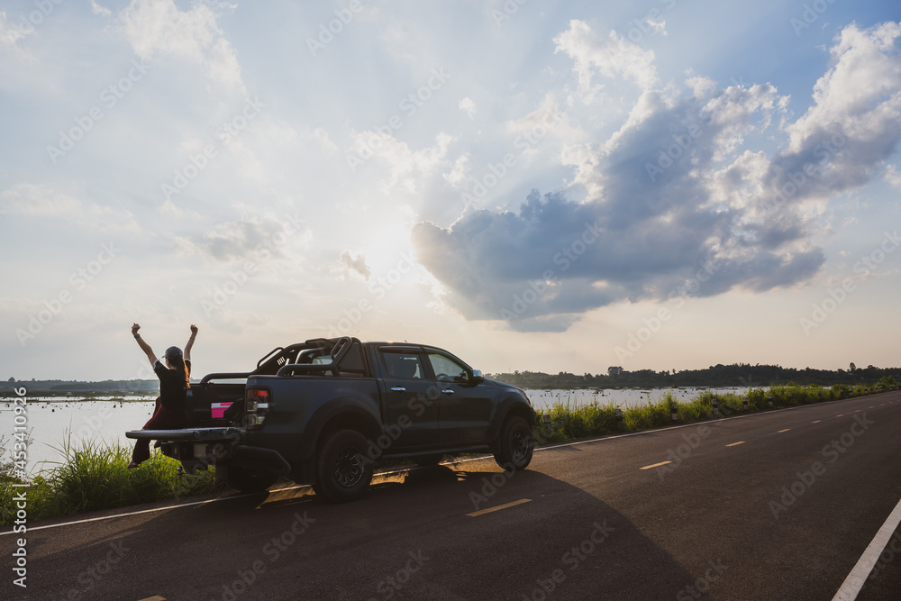 Fototapeta premium Asian female traveler camping in the back of a car with a background near a lake or river in vintage tones happy young woman traveling in summer country road girl sitting in the back of the car