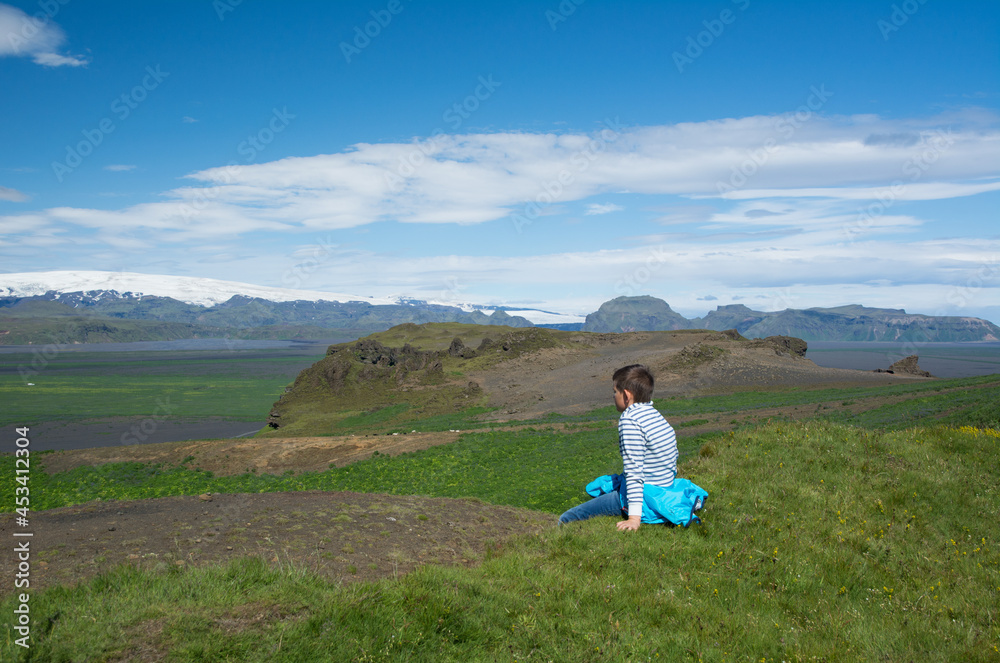 Person sitting on a grass enjoying view to the green mountains and valley, Iceland