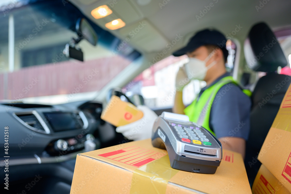 Asian male delivery driver with cardboard box on the car seat and parcel box is driving the delivery of the customers shopping online under coronavirus pandemic COVID-19