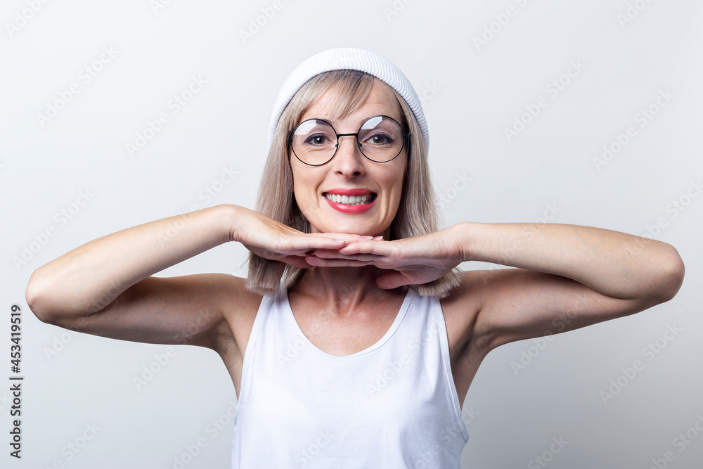 Smiling young woman holding her palms under the chin on a light background