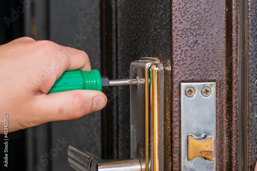 an employee changes the lock on an old iron door with a screwdriver