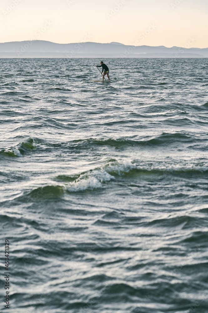 Fototapeta premium Man on sup board paddling far away