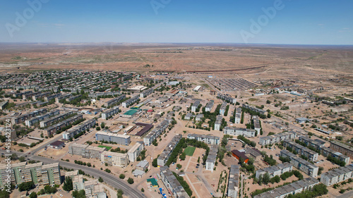 Drone view of the small town of Balkhash. The city is located on the shore of a lake. Low houses  free streets and roads. Green trees grow and there are sports grounds. There is a steppe around city