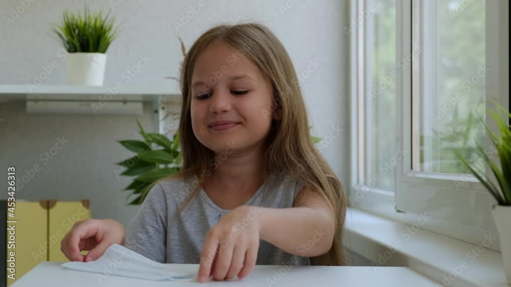 Little girl puts on a preventive medical mask indoor, concept of home quarantine. Child smiling and looking at camera Little girl puts on a preventive medical mask indoor, concept of home quarantine. Child smiling and looking at camera