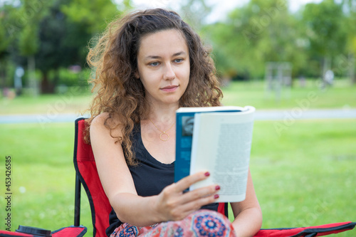 Young woman sitting on camping chair and reading a book