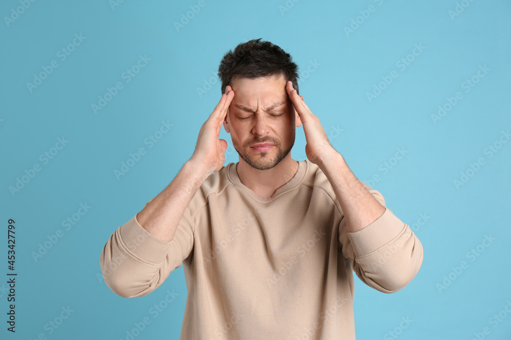 Man suffering from terrible migraine on light blue background
