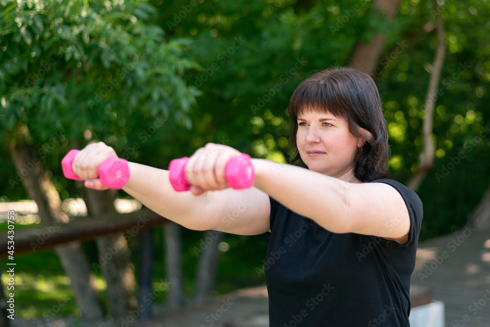Young girl is engaged with dumbbells in the park and looks ahead. Trainer shows exercise for biceps and triceps Young girl is engaged with dumbbells in the park and looks ahead. Trainer shows exercise for biceps and triceps