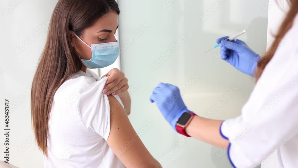 Woman in medical face mask getting Covid-19. Flu vaccine at the hospital. Professional nurse giving antiviral injection to female patient. Vaccination, disease prevention concept. Close-up of Woman in medical face mask getting Covid-19. Flu vaccine at the hospital. Professional nurse giving antiviral injection to female patient. Vaccination, disease prevention concept. Close-up of