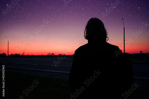 Dark silhouette of a young man looking on the stars and beautiful colorful sundown. Night time, underexposed picture. © Valerie